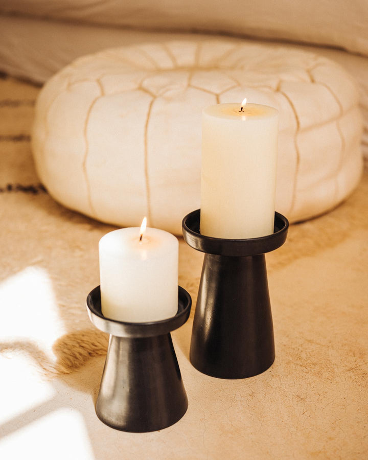 Two white candles in black holders on a textured surface with a blurred background