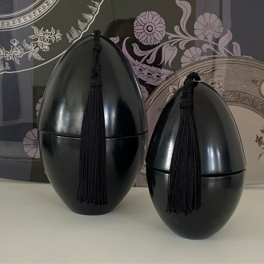Two black decorative items with tassels on a white surface, with a decorative background.