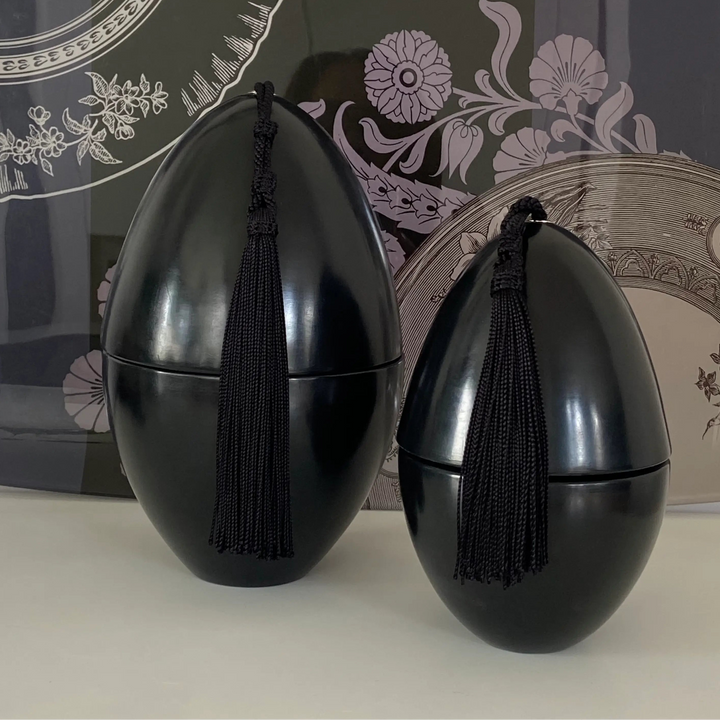 Two black decorative items with tassels on a white surface, with a decorative background.