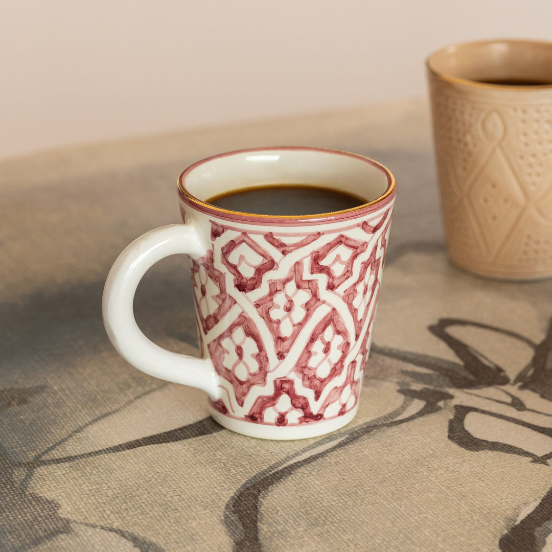 Red and white patterned mug with a beige textured mug on a stone surface.