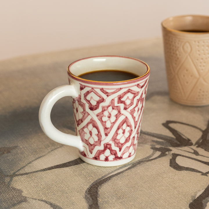 Red and white patterned mug with a beige textured mug on a stone surface.
