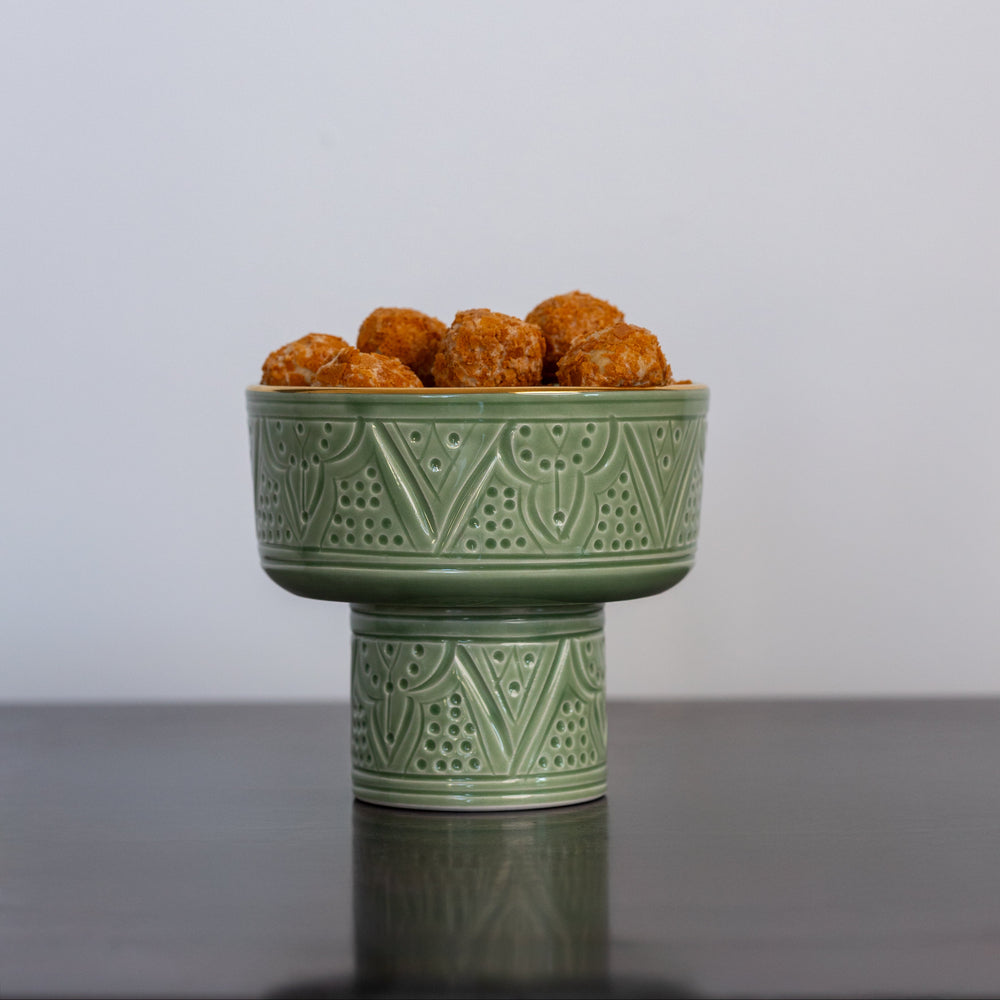 Green ceramic bowl with decorative patterns containing small round objects on a gray surface and light gray background