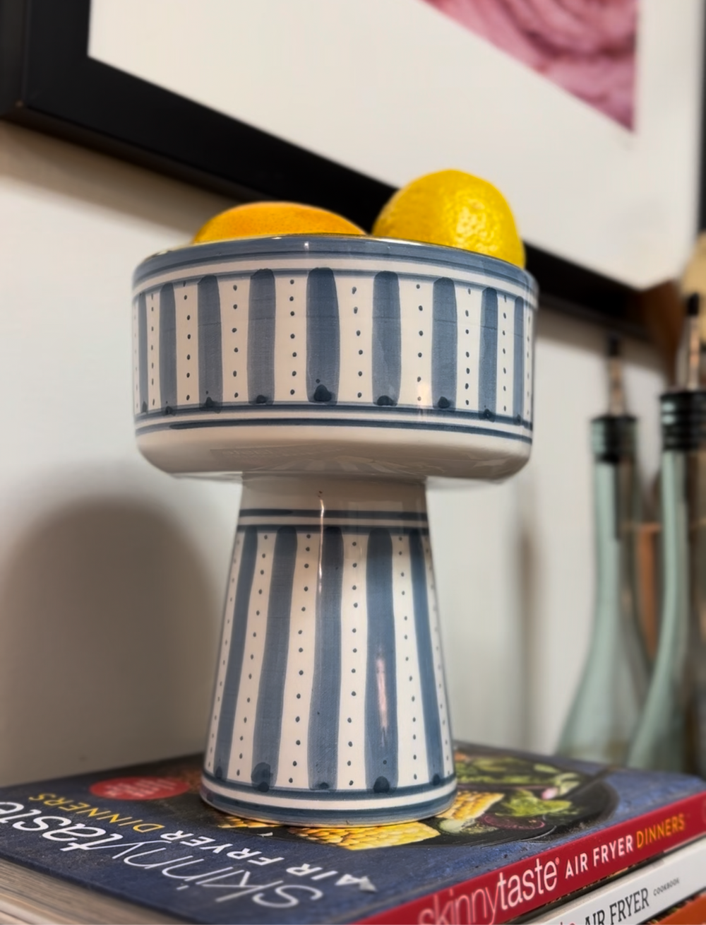 Ceramic fruit bowl with blue and white stripes containing lemons on a bookshelf.