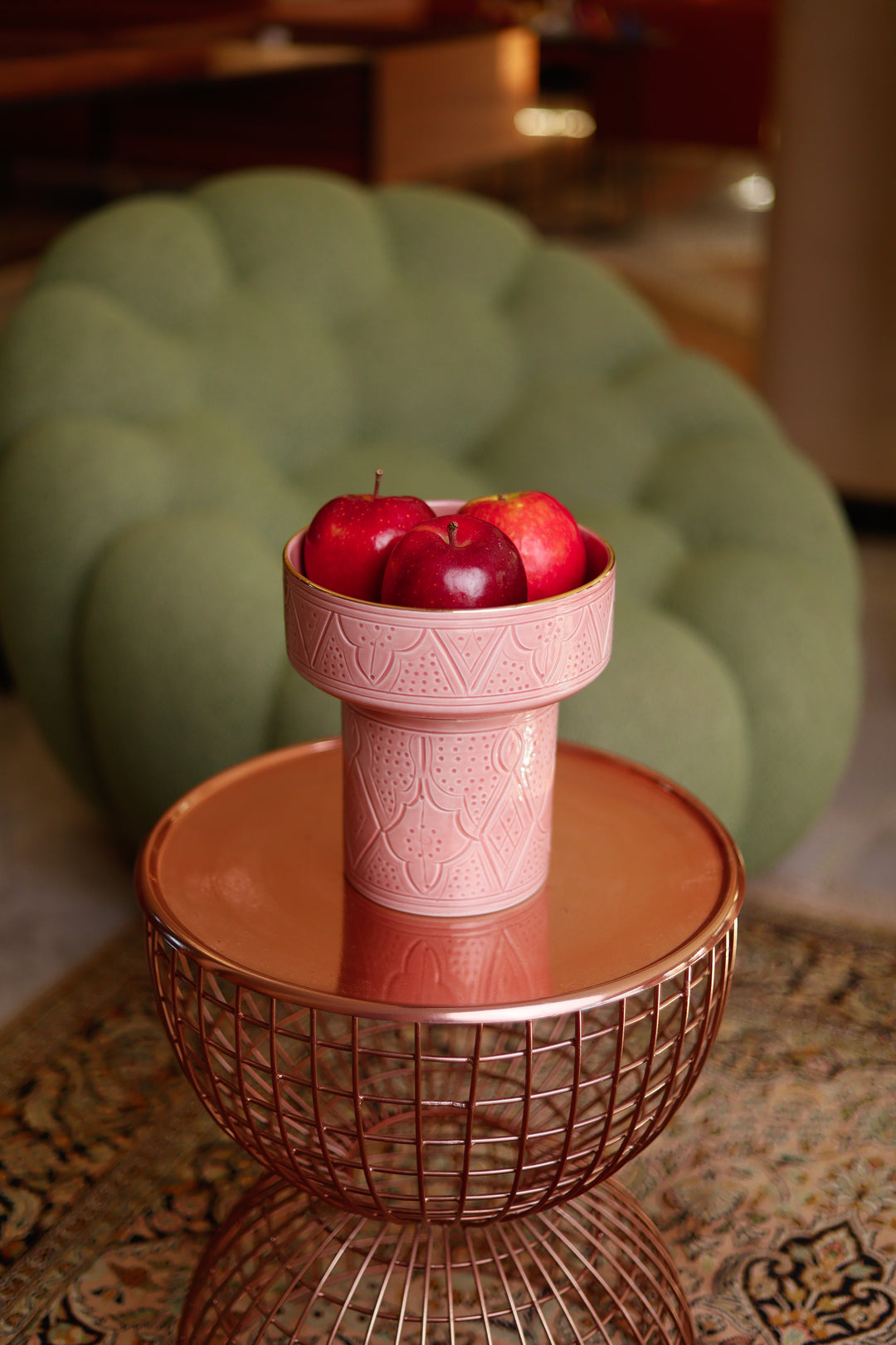 Pink decorative bowl with apples on a small round table in a room.