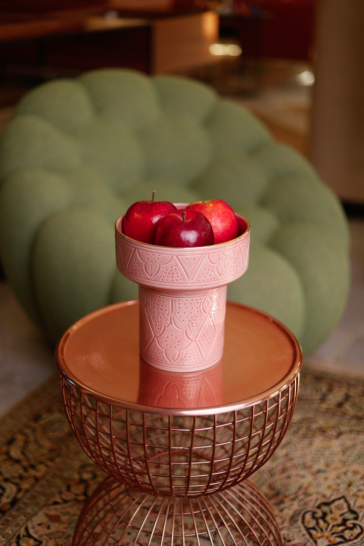 Pink decorative bowl with apples on a small round table in a room.