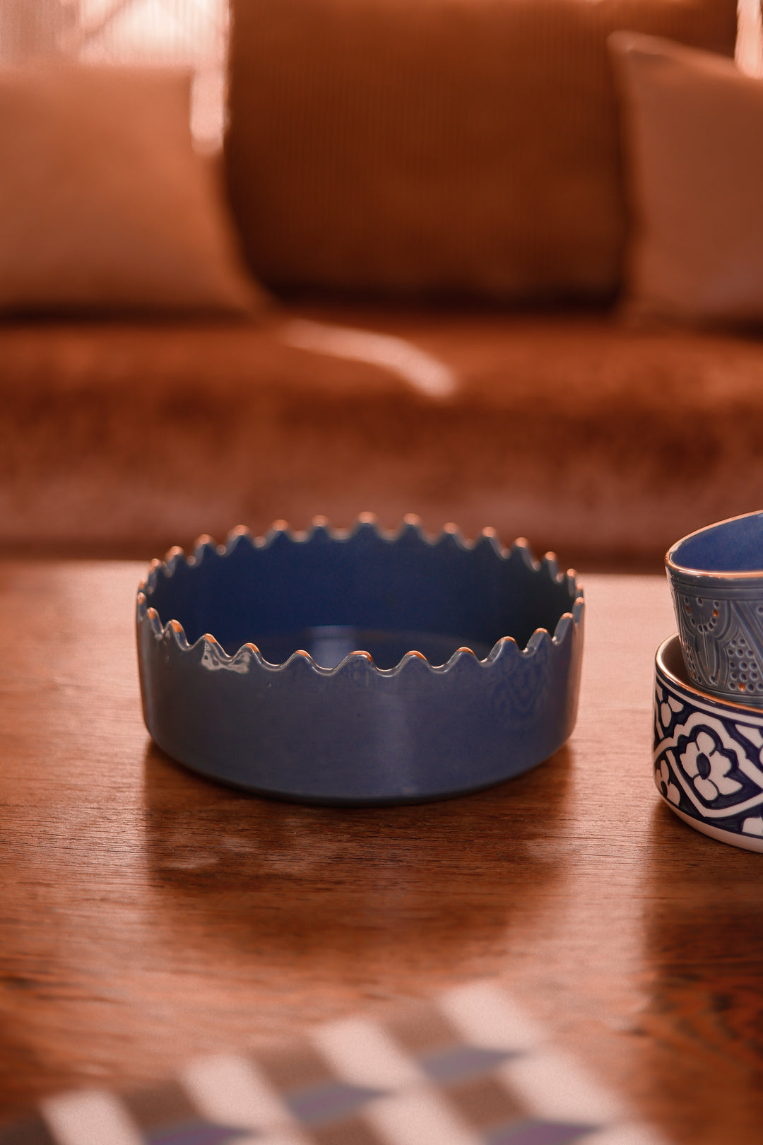 Blue ceramic bowl on a wooden table with a blurred brown sofa in the background