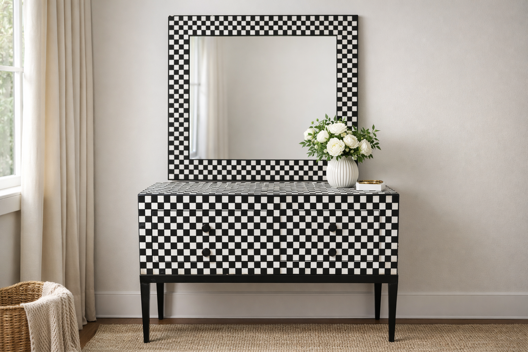 Black and white checkered dresser with mirror in a room with a window and vase of flowers.