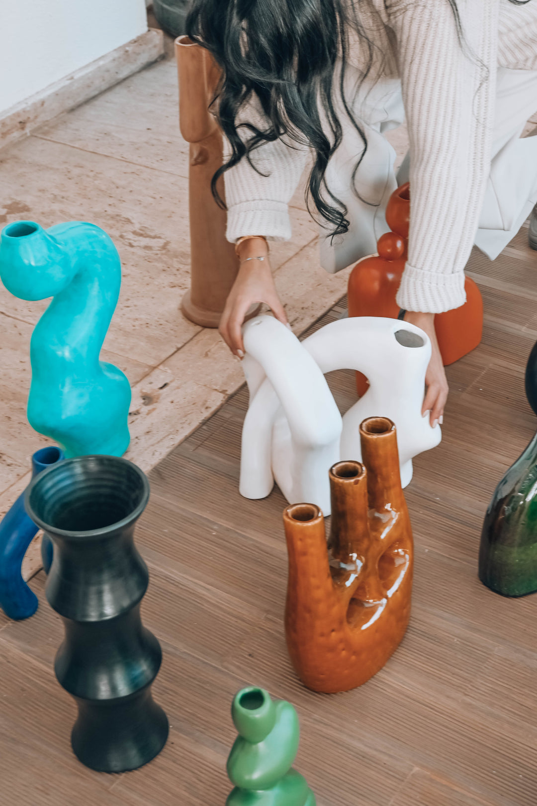 Person arranging colorful ceramic vases on a wooden floor