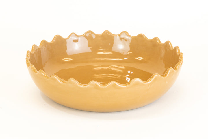 Beige ceramic shallow dish with wavy edge on a white background
